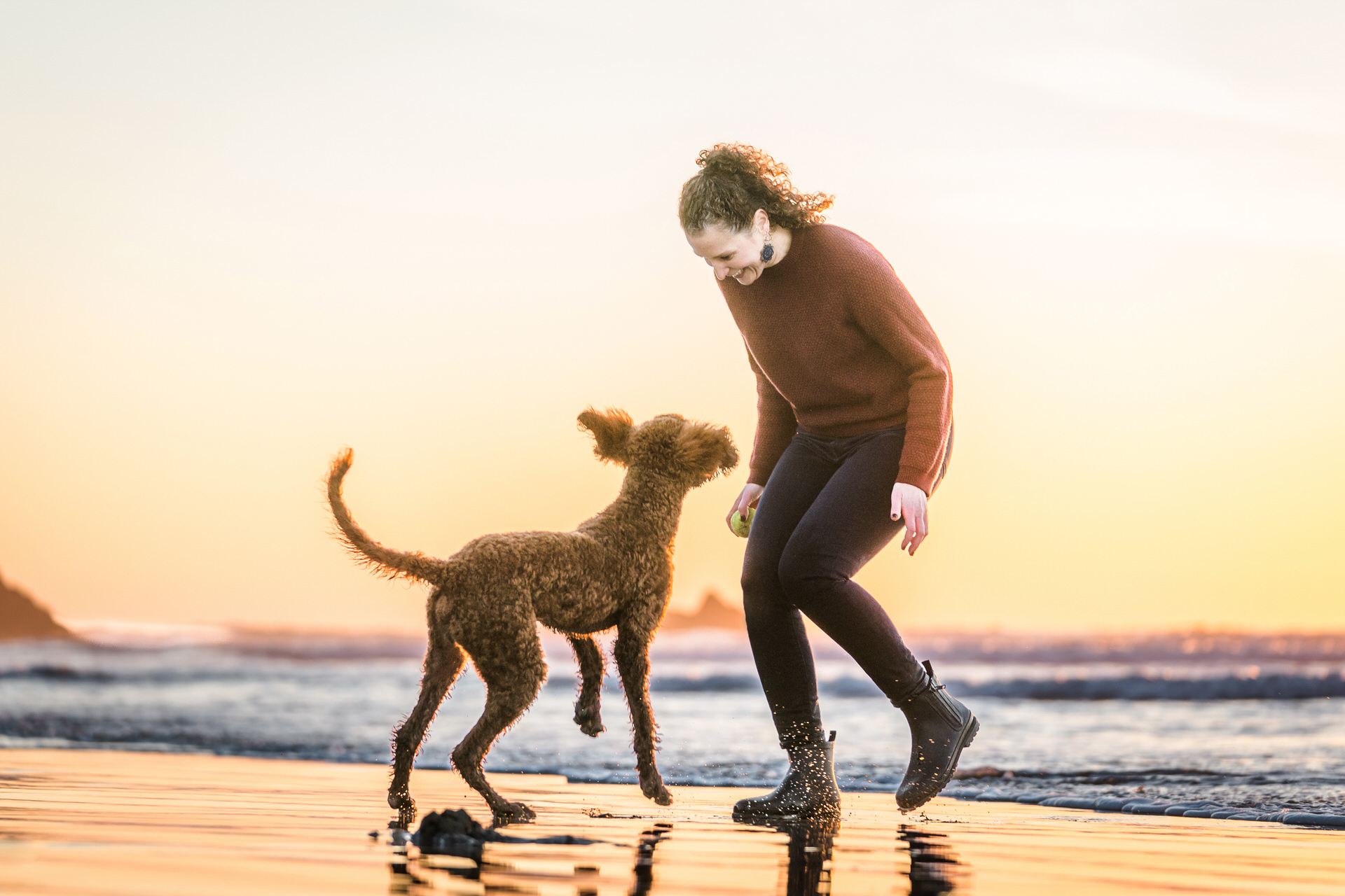 woman playing with goldendoodle dog at sunset