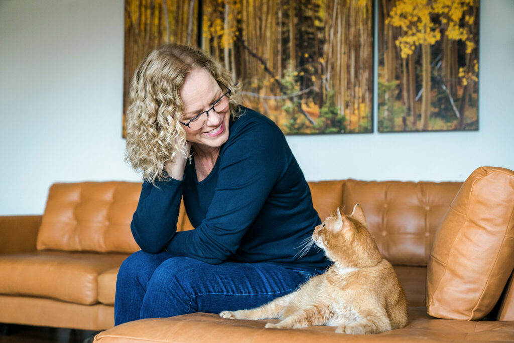 Woman and orange cat look at each other while sitting on a couch