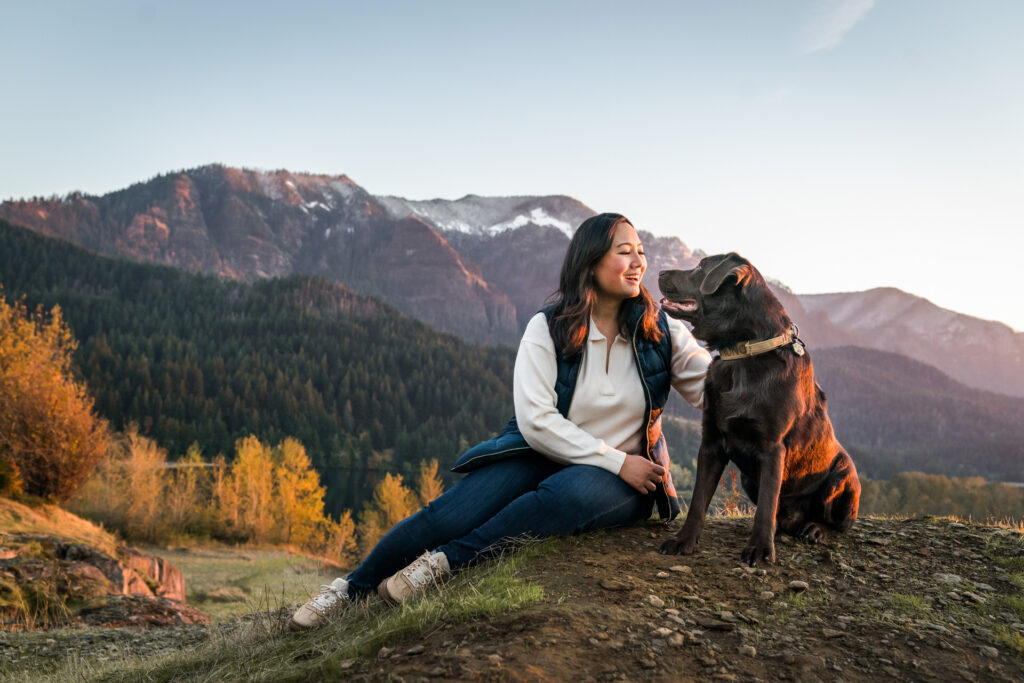 Woman and dog look at each other in beautiful location with mountains and fall colors