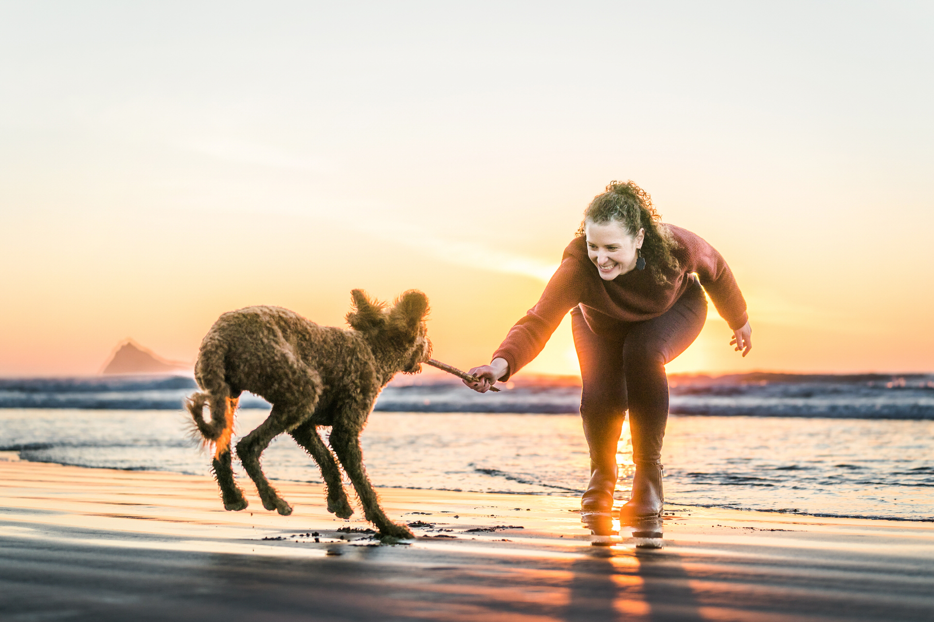 woman plays with dog at sunset at the beach
