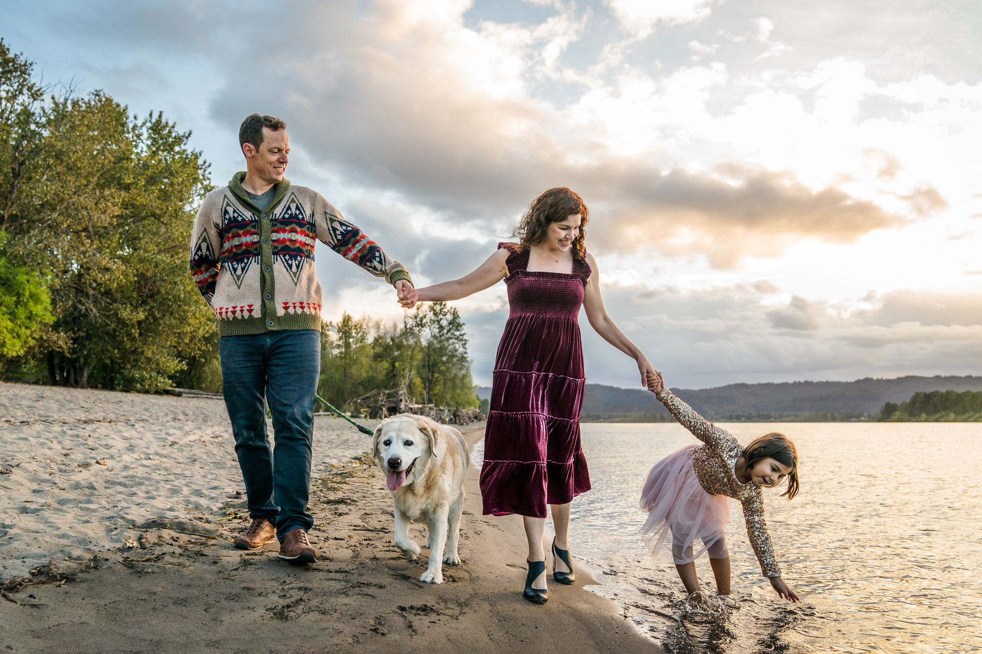 Family with dog and child walk along river beach in Portland, Oregon.