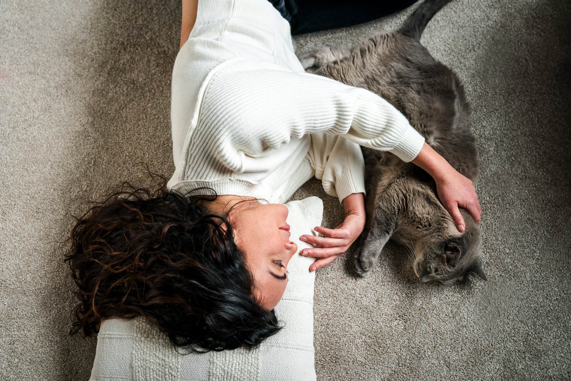 Woman laying with cat on carpet.