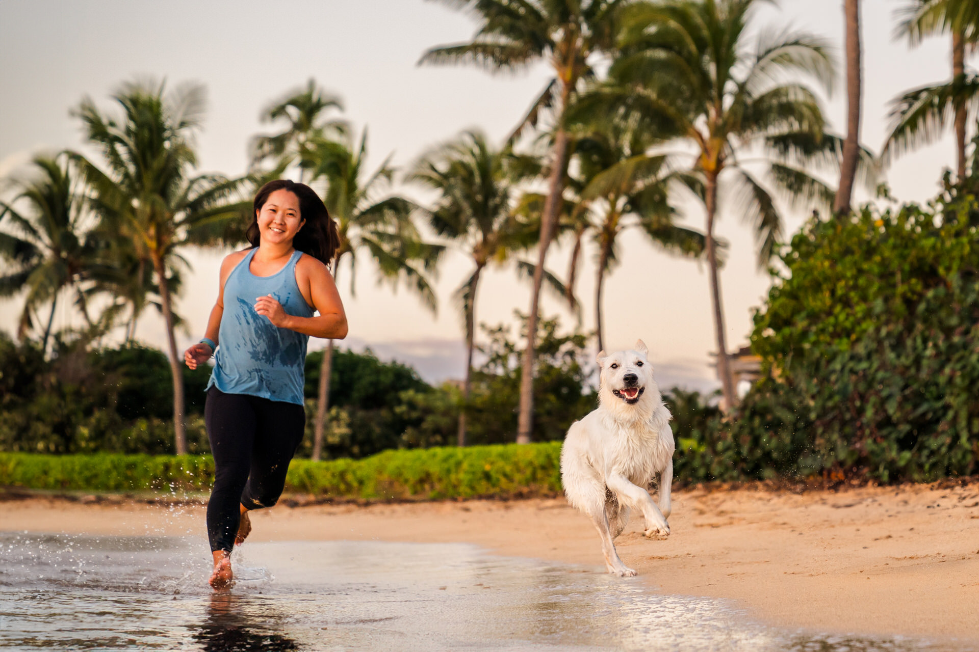 Woman and dog running on beach at sunset.