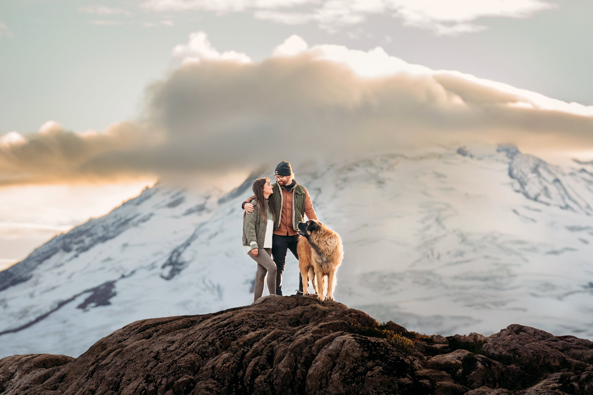 couple with dog look at each other while standing in front of Mt. Baker 